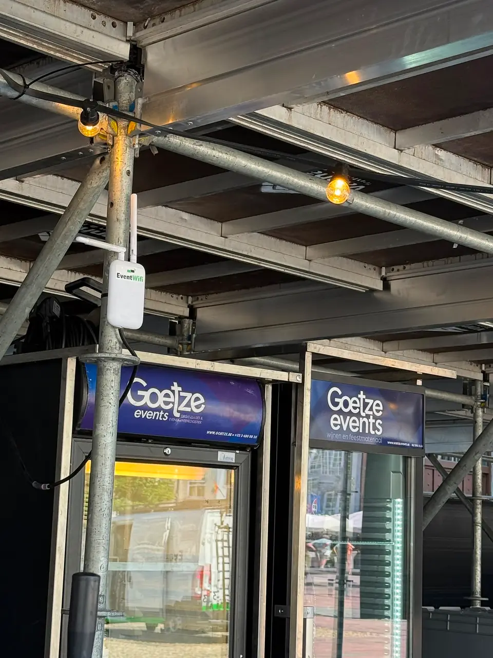 Wifi accesspoint van EventWiFi gemonteerd tegen een muur onder een boom op een stadsfeest