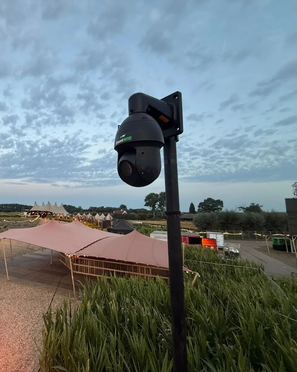 Bestuurbare PTZ camera van EventWiFi op een mast met daarachter het festivalterrein bij valavond