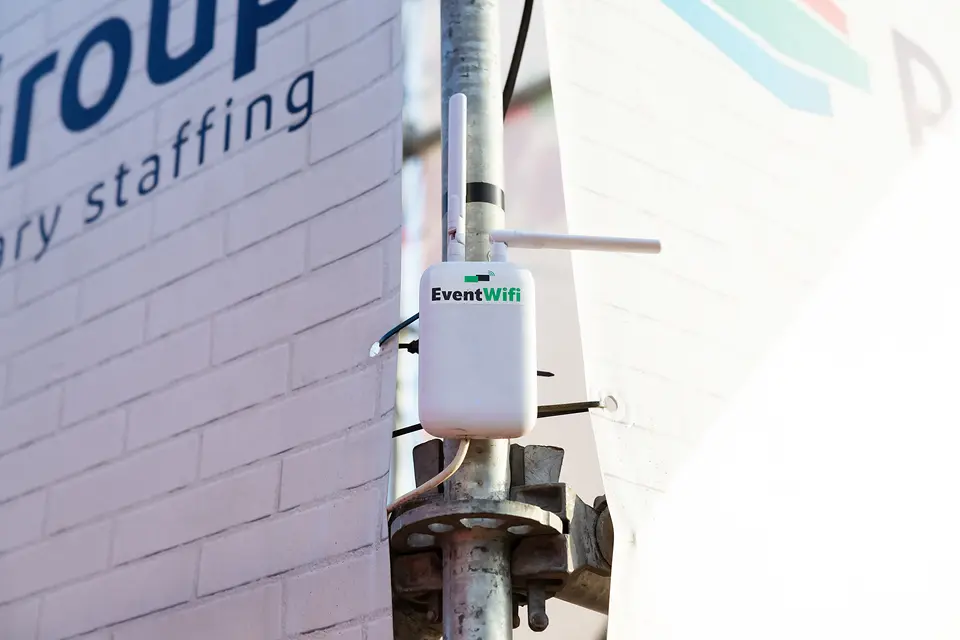 Accesspoint van EventWiFi op een stellingbuis tegen de hoek van een gebouw op Rijvers Festival