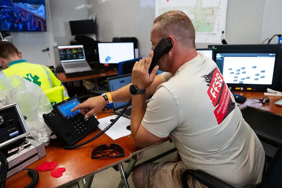 Coördinator van de veiligheidsdienst belt vanuit de controlekamer van Rijvers Festival, met de camerabeelden binnen handbereik