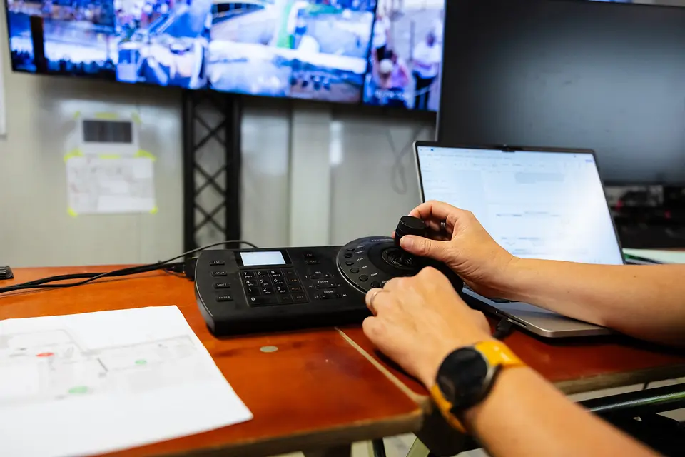 Bediening van de camera's met een joystick, met de wand vol live camerabeelden erachter
