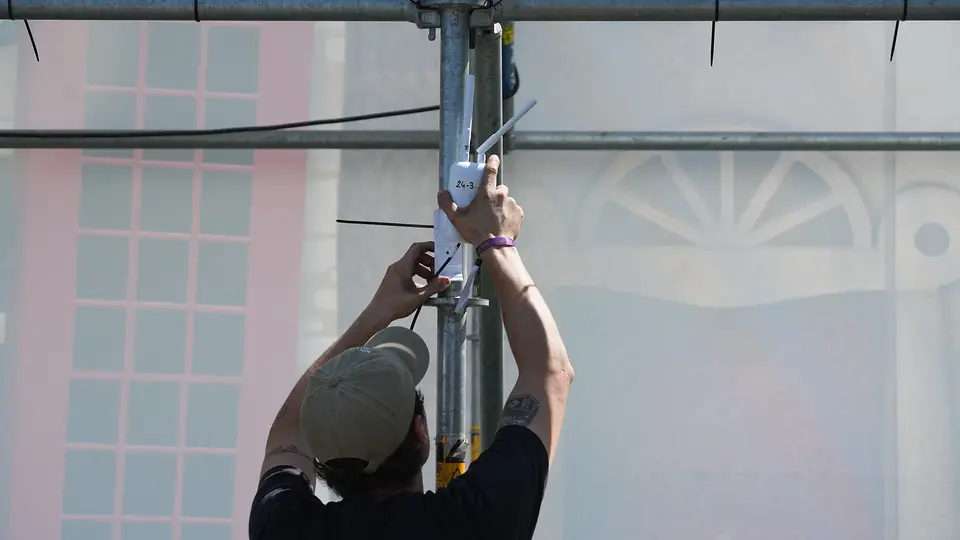 Technieker van EventWiFi monteert een accesspoint op een paal tijdens de opbouw van een evenement